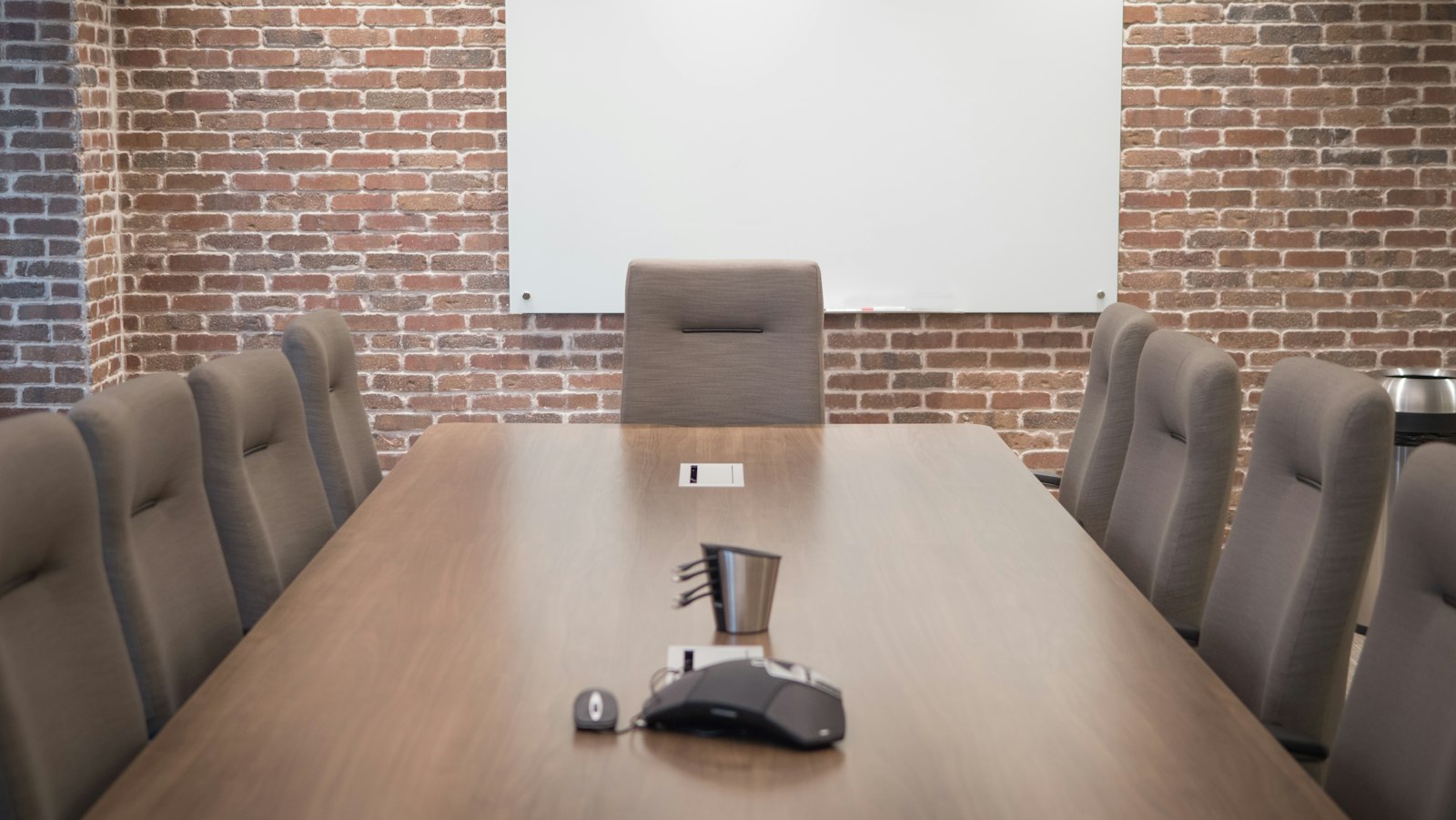 Salle de réunion avec une table en bois, un fauteuil et un écran blanc sur un mur de briques