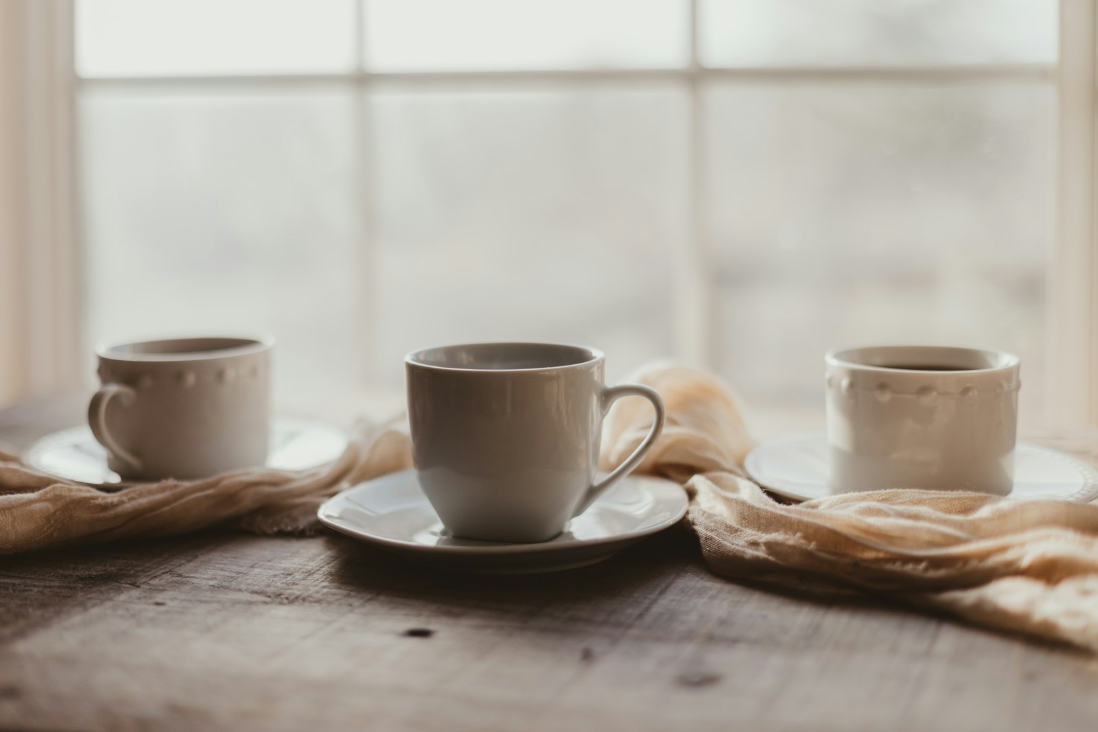 Trois tasses de café sur une table en bois, devant une fenêtre lumineuse