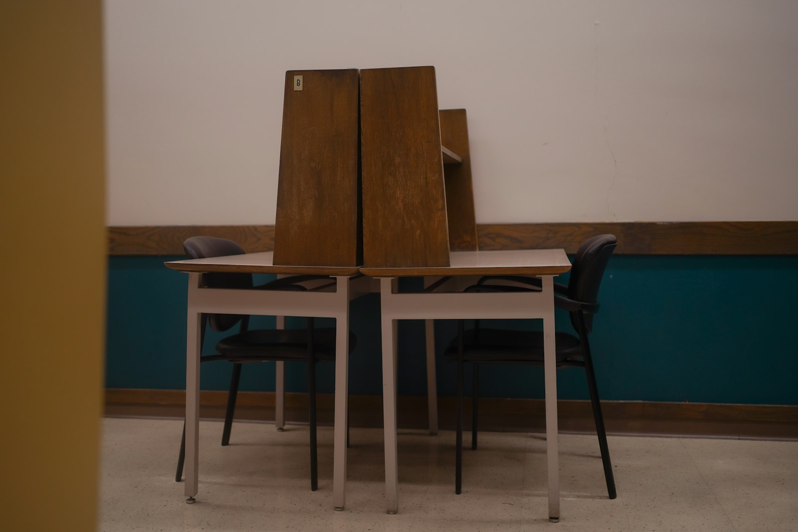 Deux bureaux accolés séparés par une cloison en bois, chacun avec sa chaise, devant un mur bleu-vert